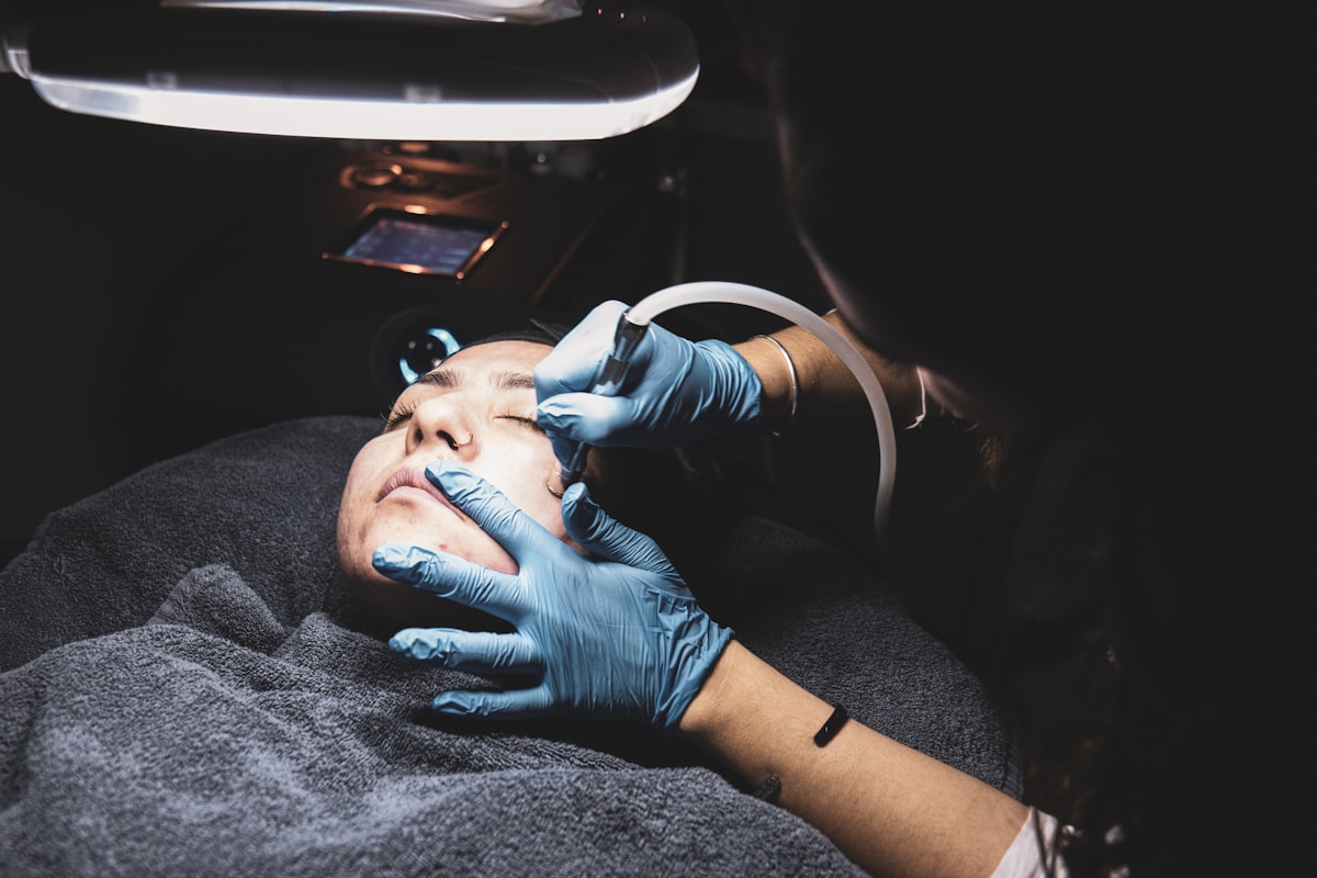 Deep-cleansing extraction procedure with gloved professional working on woman under treatment lamp